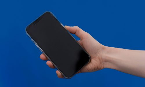 Close-up of a hand holding a smartphone against a bright blue background, showcasing modern technology.
